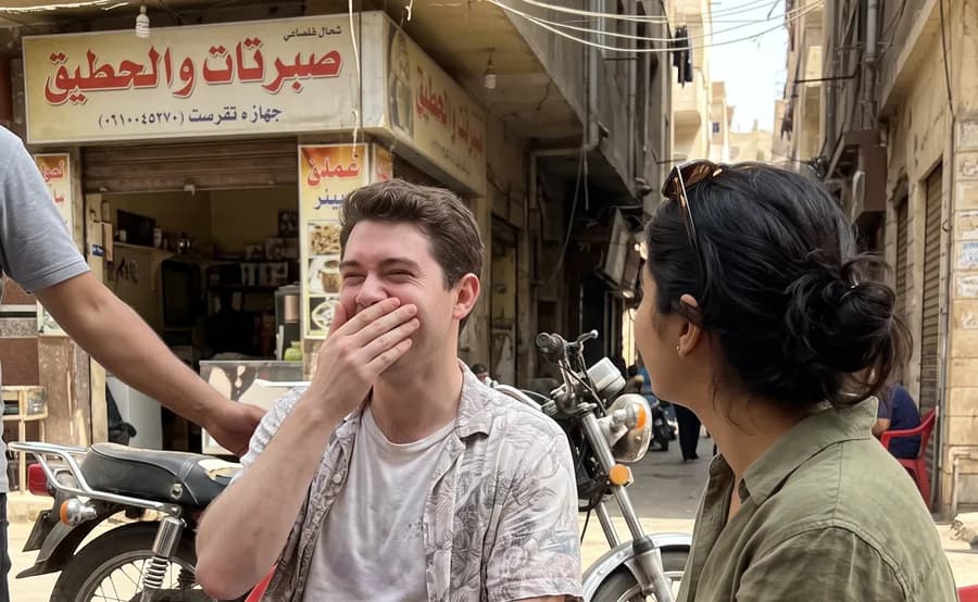 He laughs with his hand over his mouth at a street coffee house, she sits across from him